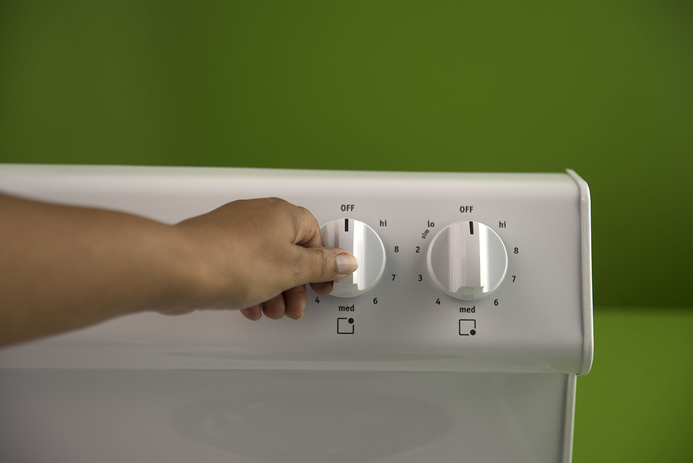 A woman turning the stove knob to the off position.