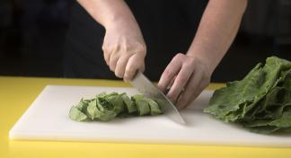 A woman cutting washed, leafy greens that have been rolled for slicing on a white cutting board.