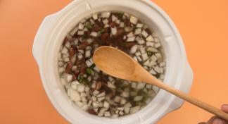 Wooden spoon positioned over a crock pot of beans, garlic, jalapenos, and onions