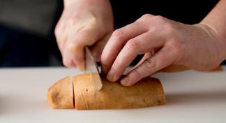 Hands chopping sweet potato on chopping board with knife