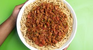 Hands presenting bowl of spaghetti topped with tomato and meat sauce