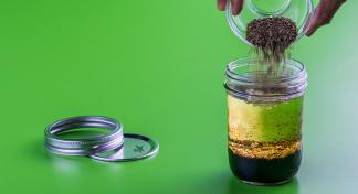 Hand pouring contents of bowl into a jar to make salad dressing