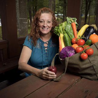 A woman sitting at a table with a bag of fresh fruits and vegetables.